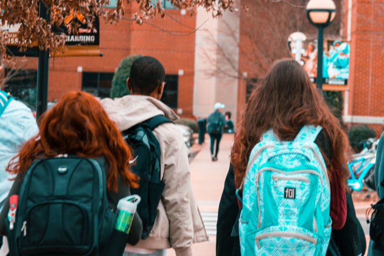 Five teens walking towards a building with backpacks