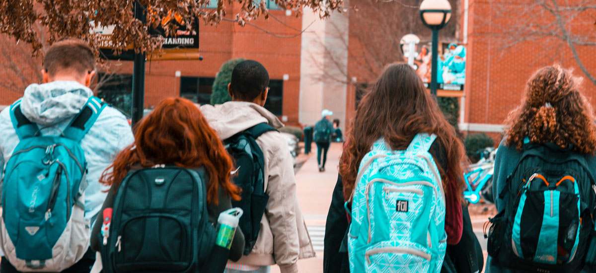 Five teens walking towards a building with backpacks