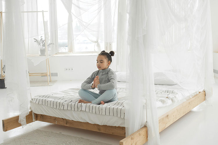 Child sitting on bed with crossed legs and closed eyes