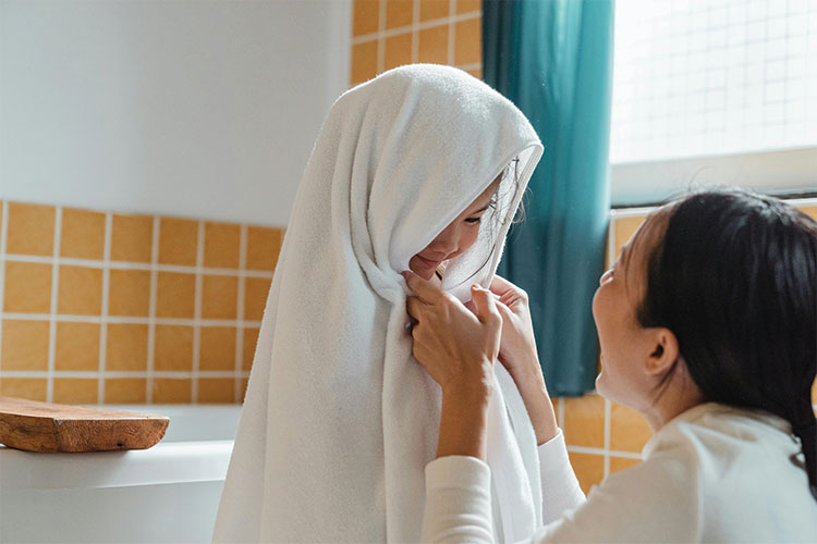 Happy parent drying child with fluffy towel in bathroom