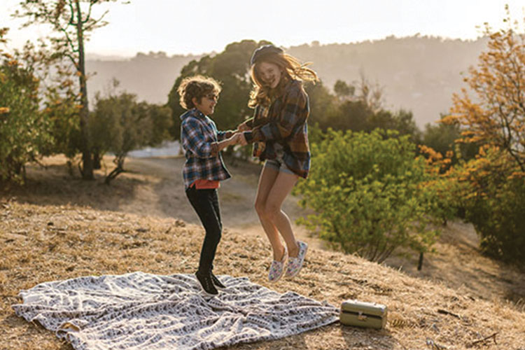 Two kids jumping up and down on a picnic blanket in the woods