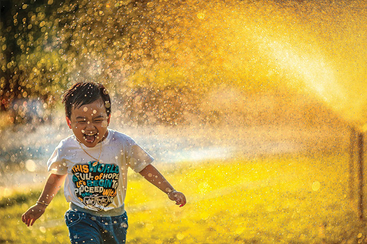 child running through a sprinkler in the sunlight